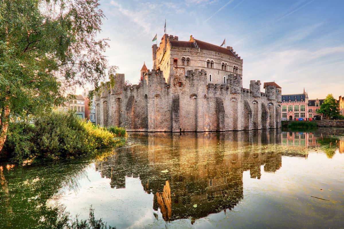 Un lago con vegetación reflejando los muros defensivos del castillo de Gante