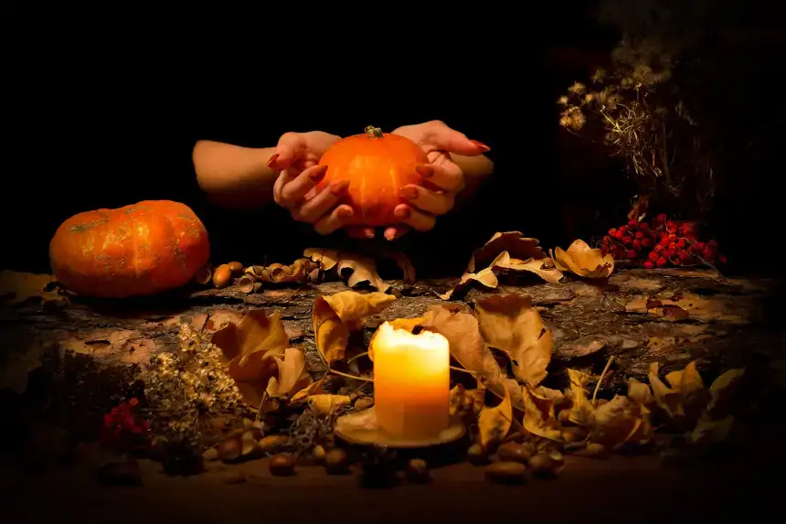 Une citrouille dans les mains d'une femme et une bougie à côté de feuilles mortes