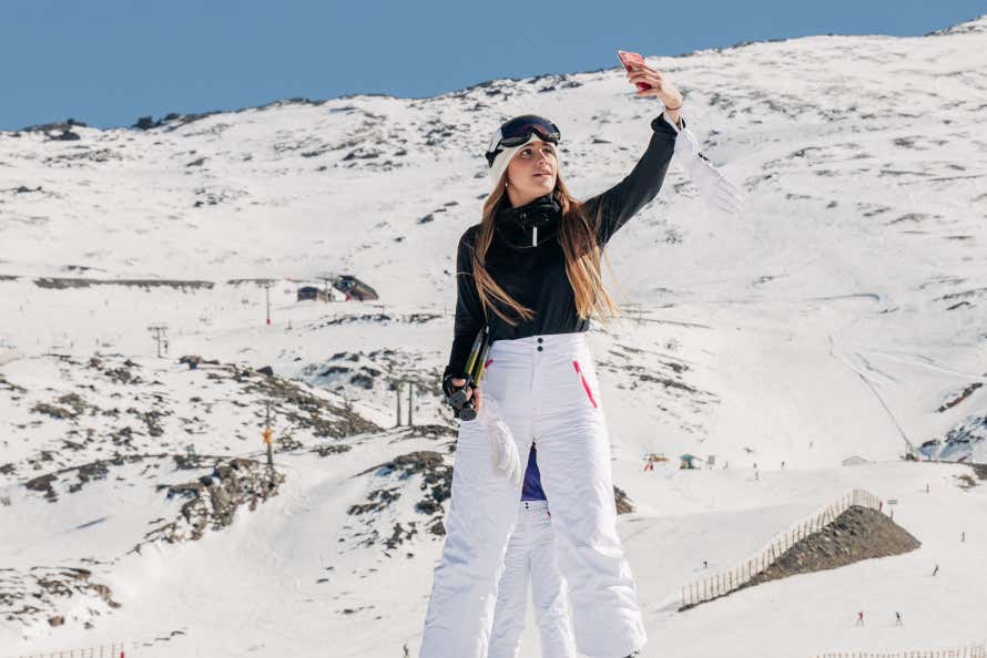 Una chica se hace un selfie con un móvil. Se observan unas montañas nevadas de fondo