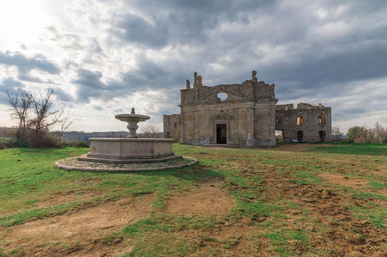 I resti di una fontana ottagonale davanti ai ruderi di un'antica chiesa barocca in uno spiazzo d'erba in un giorno nuvoloso