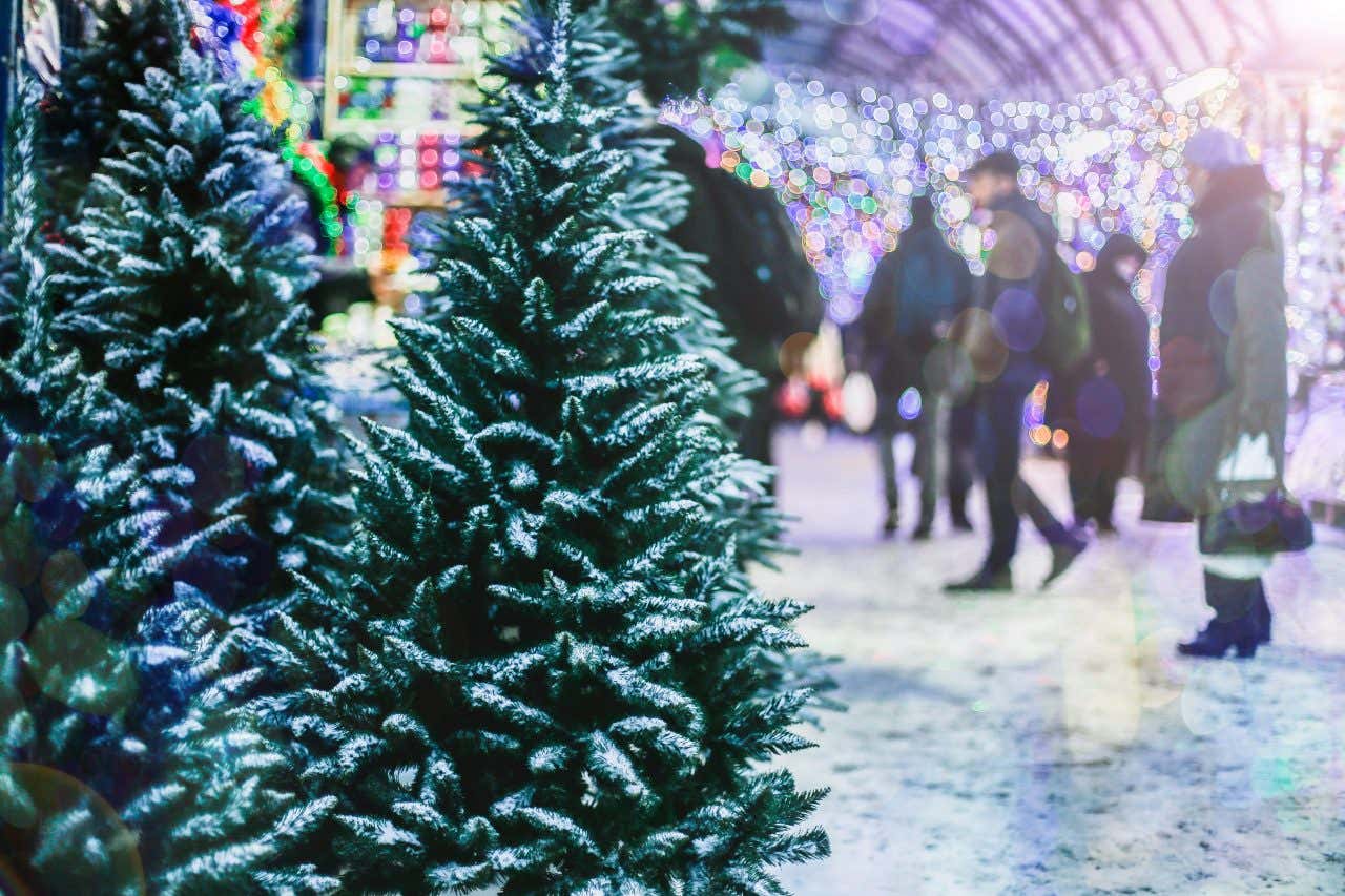 Passants dans un marché de Noël de New York avec des sapins enneigés au premier plan