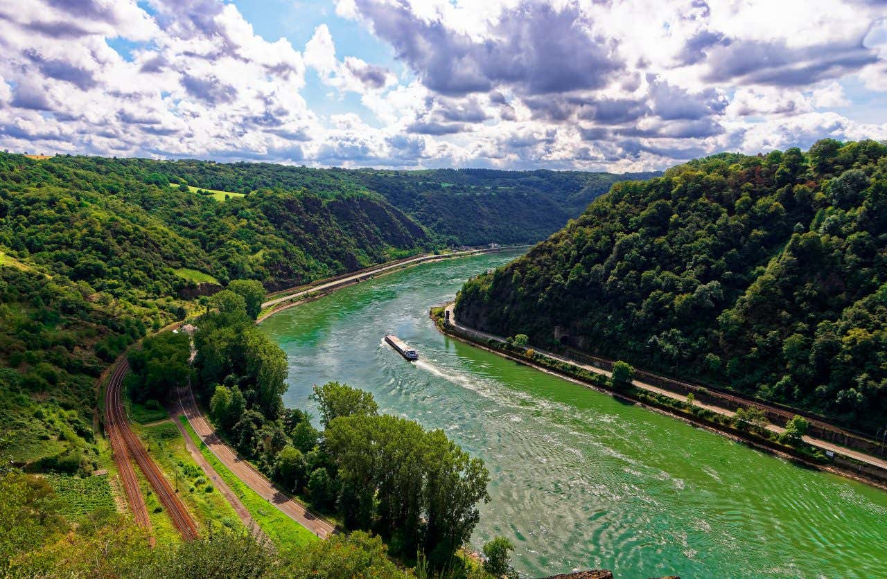 Overhead view of the lush, green Rhine Valley and River on a sunny day, verdant trees on either side of the river, a boat sailing up