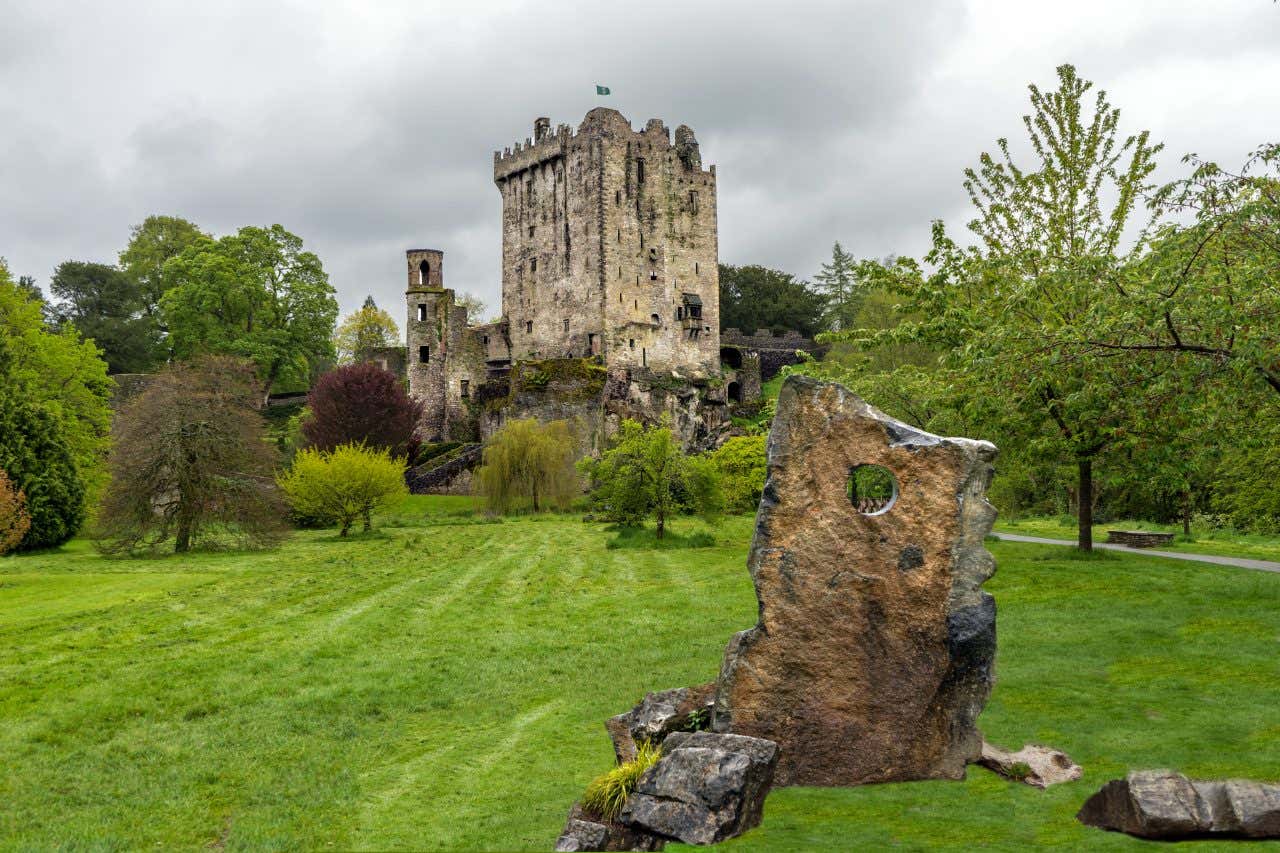 Un castello in Irlanda circondato da vegetazione sotto un cielo nuvoloso e una pietra in primo piano