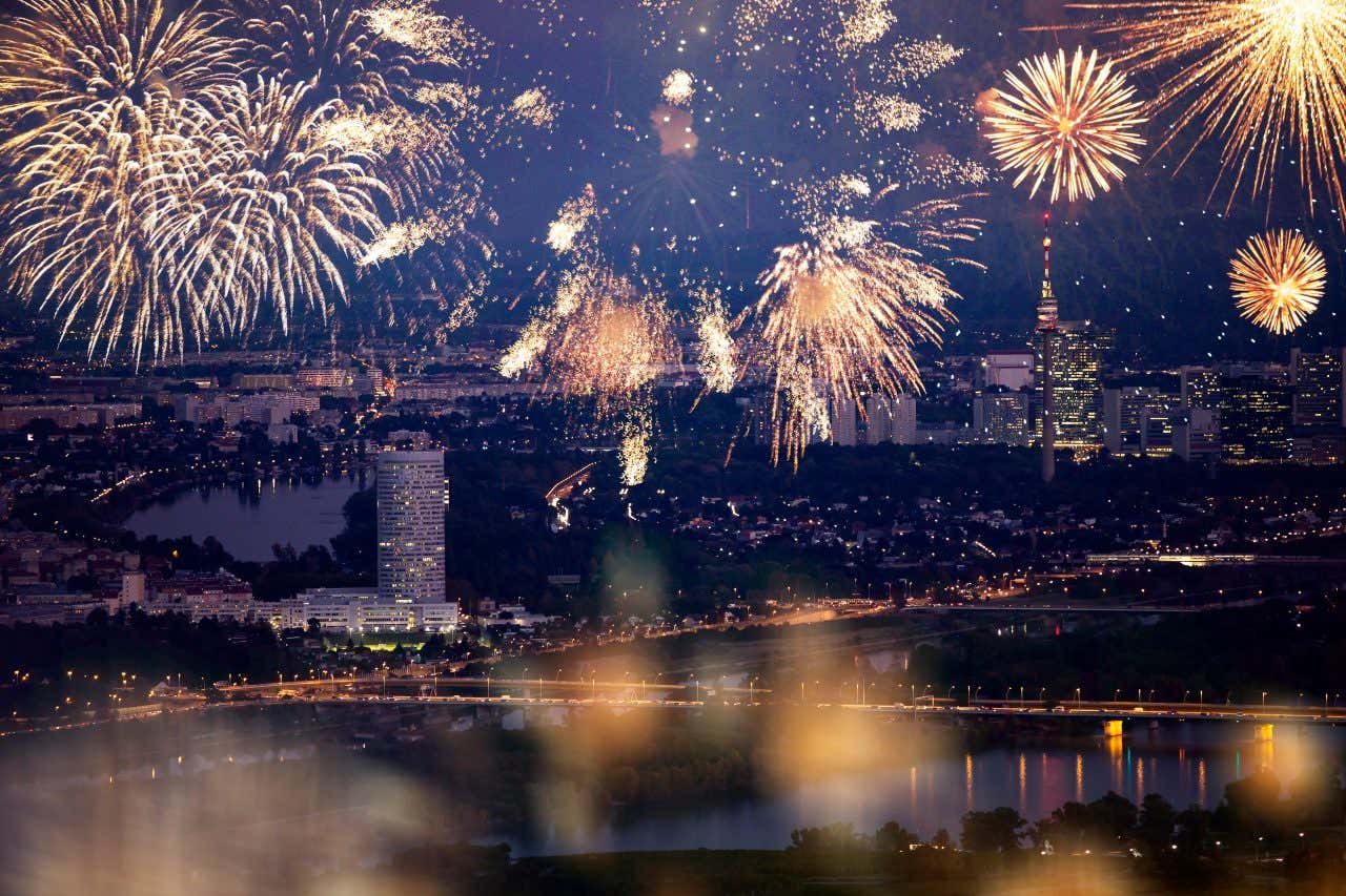 Una città di notte con un fiume che l'attraversa, illuminata totalmente da fuochi d'artificio color oro