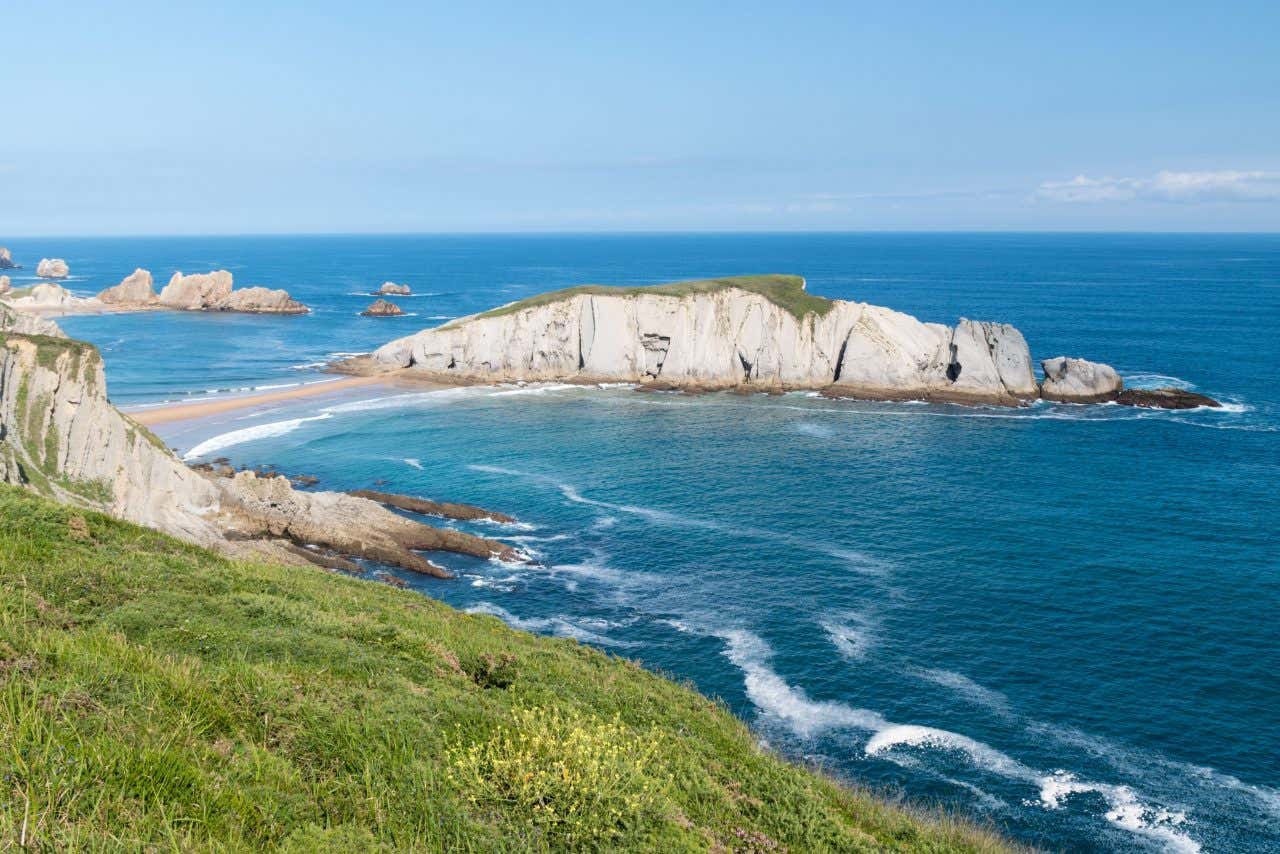 Panoramic view of the Cantabrian coast on a sunny day, rock formations spreading into the sea, waves crashing against the rock cliffs