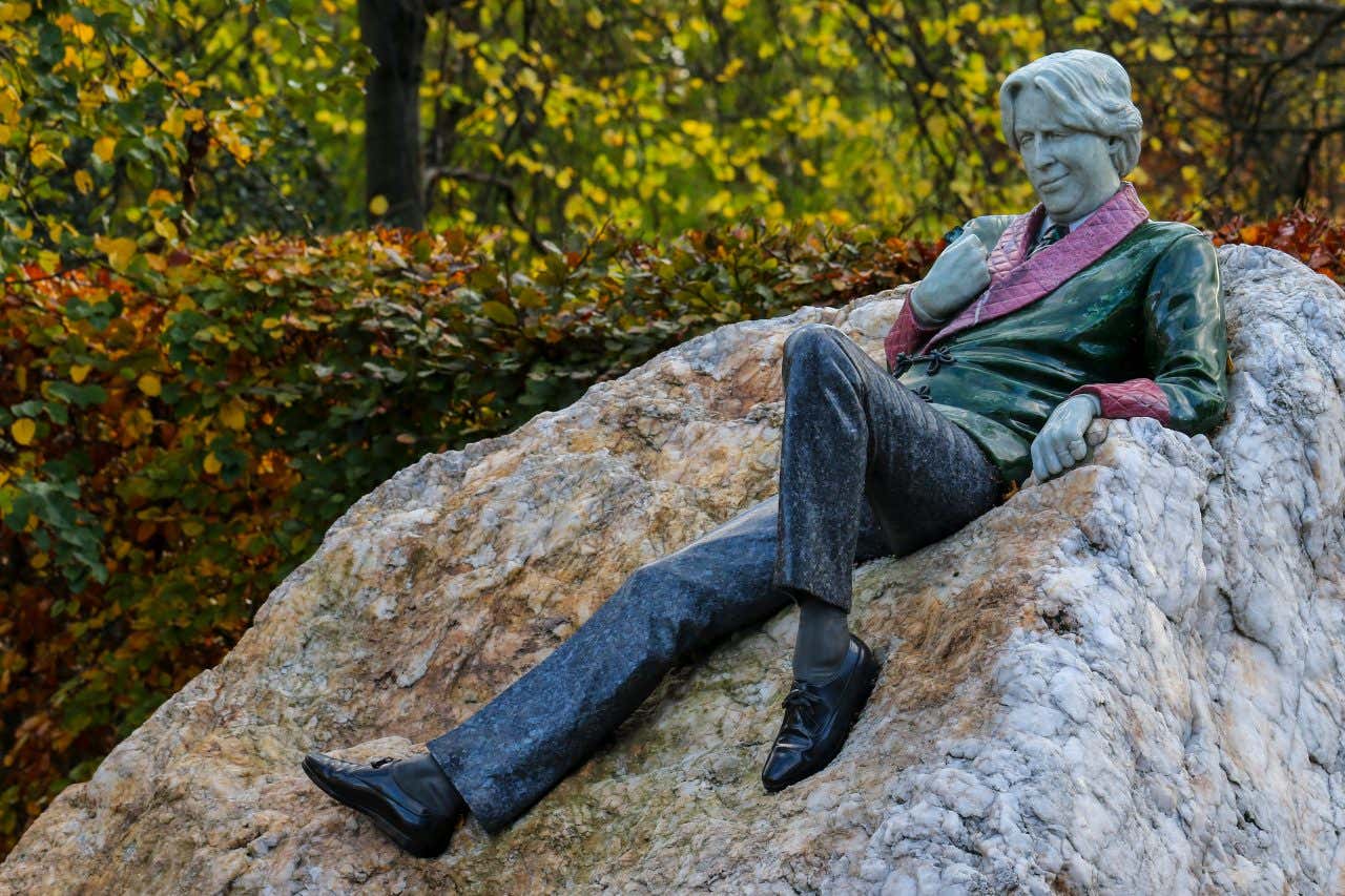 Statua di Oscar Wilde adagiato sdu una roccia con alberi sullo sfondo