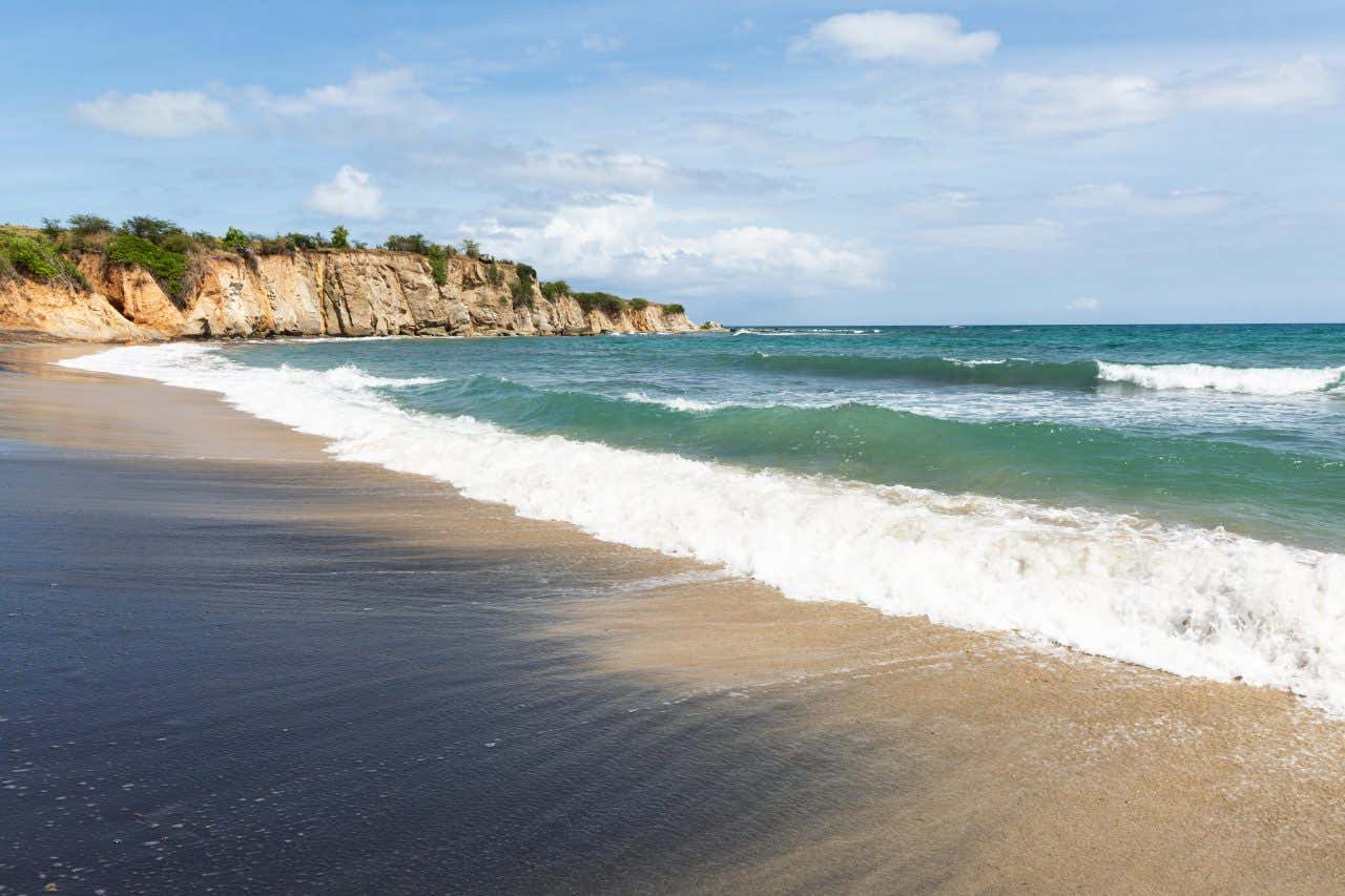 Black Sand Beach in Puerto Rico, with a merging of black and gold sand, and lined by cliffs.