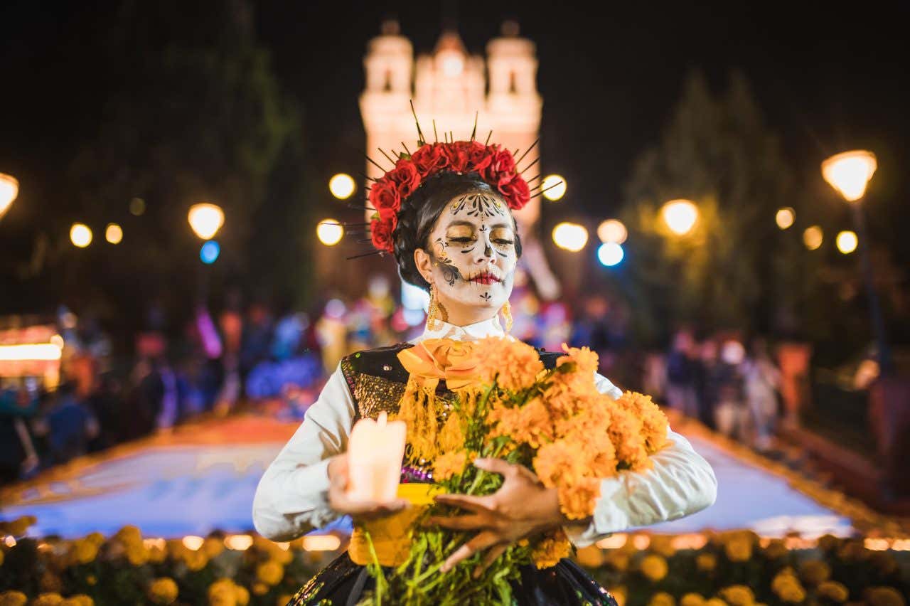 Famille maquillée et habillée en calavera avec des fleurs rouges sur la tête, portant des fleurs orange et une bougie