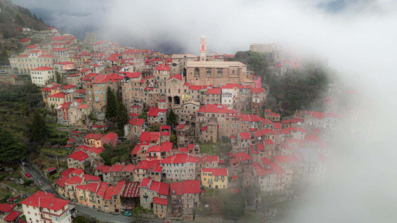 Un piccolo borgo dai tetti rossi ripreso dall'alto immerso nel verde e nella fitta nebbia