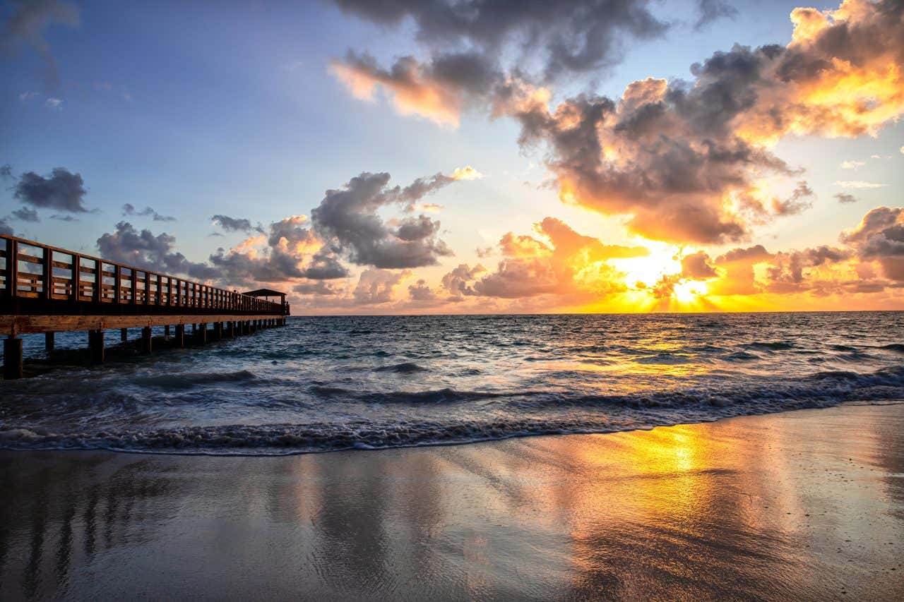 A beach in Punta Cana at sunset with a wooden pier on the left