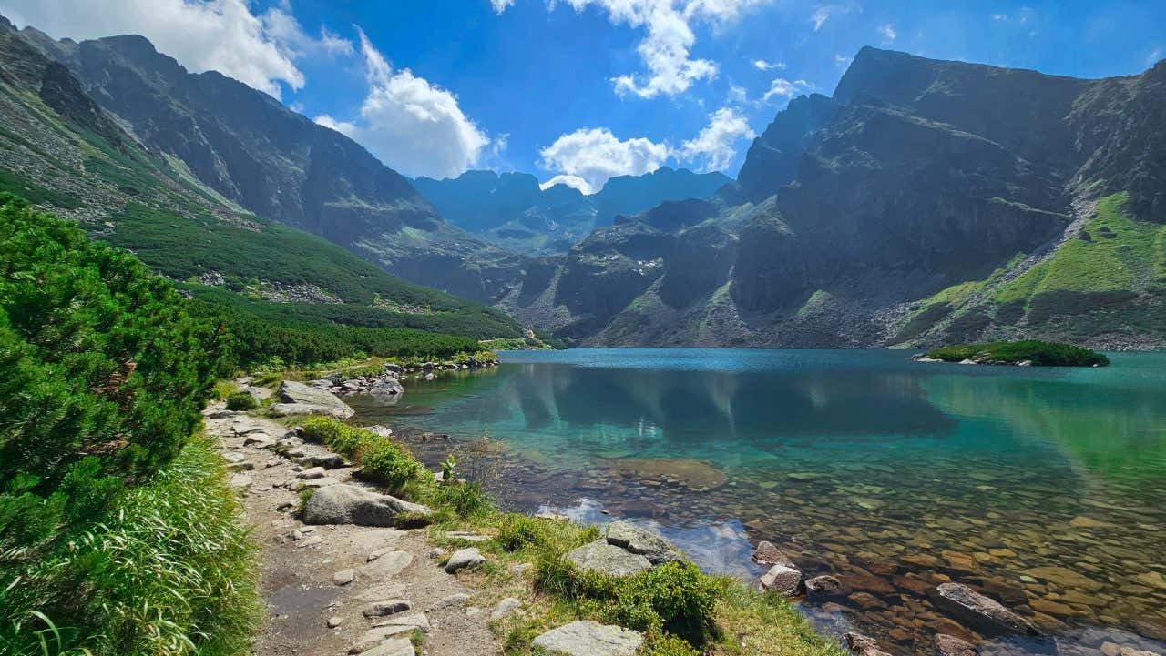 Vue panoramique sur un lac aux eaux turquoise entouré de montagne sous un ciel bleu avec quelques nuages, un incontournable à visiter depuis Cracovie