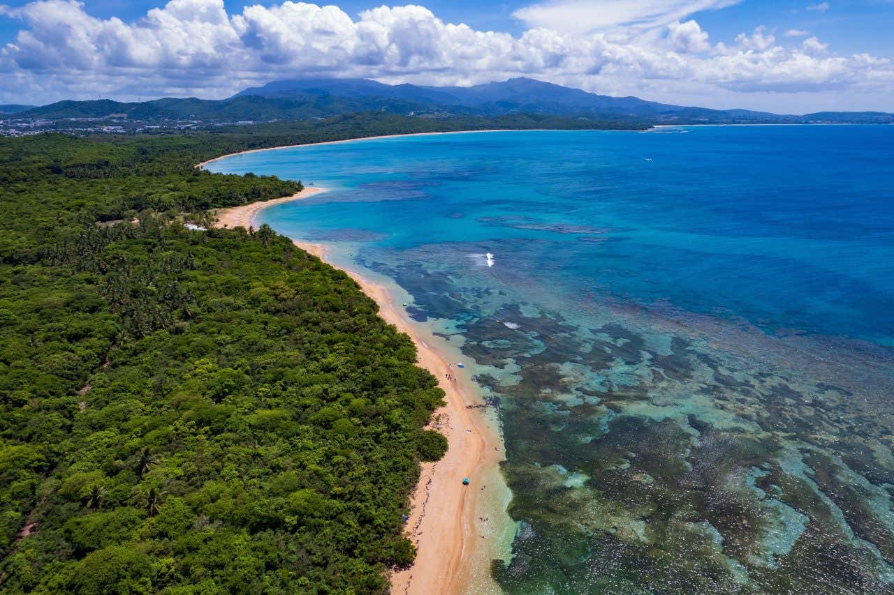 Escondida Beach as seen from the sky, with the seabed visible through the clear water.