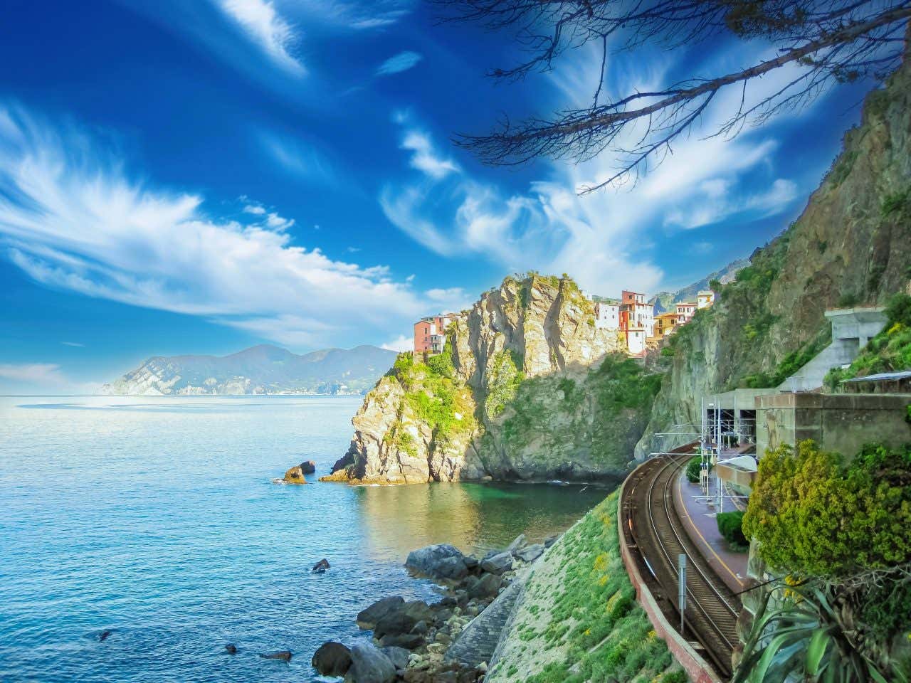 View looking out at a rocky island with houses on top between the rock formations stretching into the sea, a train track visible in right corner