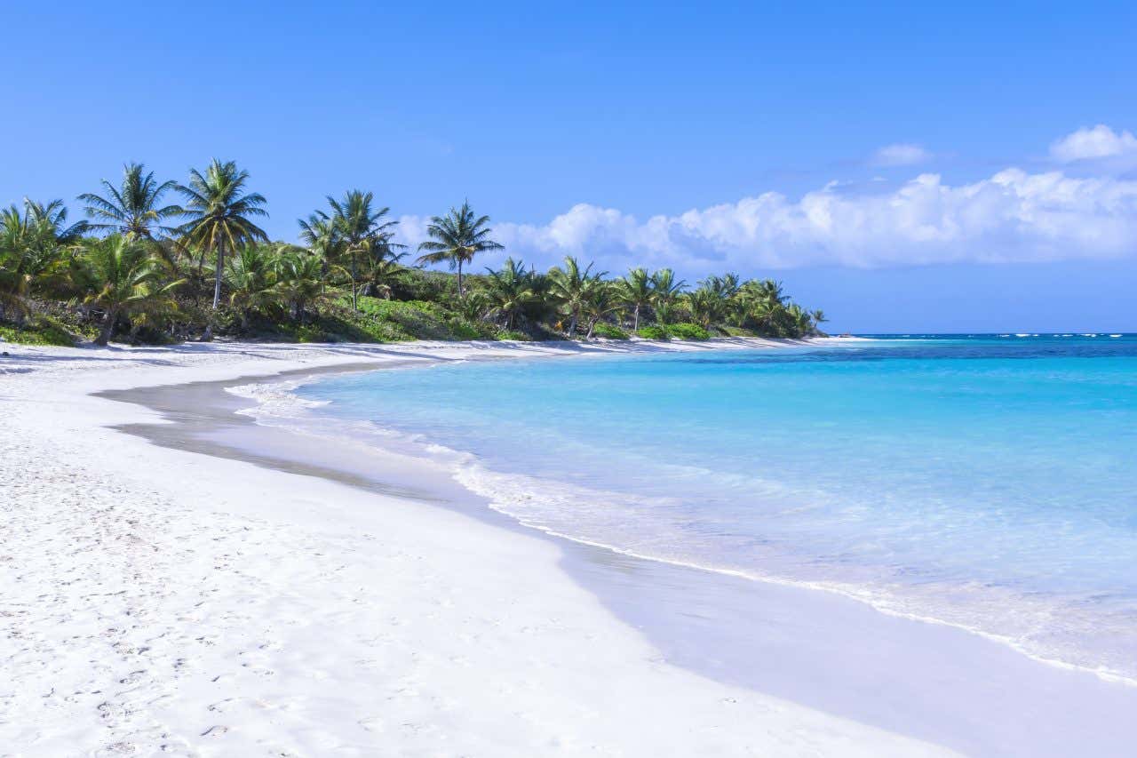 Flamenco Beach in Puerto Rico, with white sand and light blue waters, with a cloudy blue sky in the background.