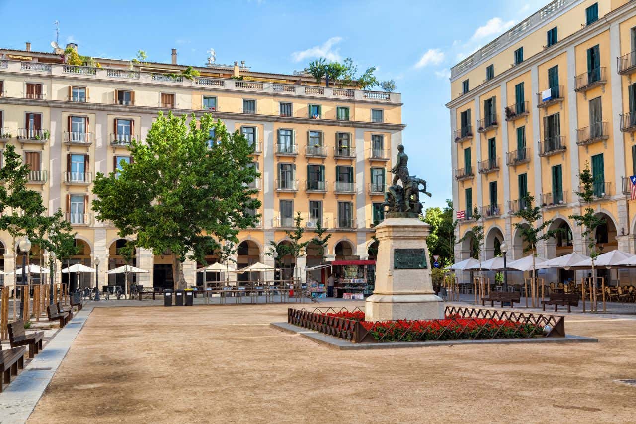 Place bordée par des bâtiments de style néoclassique à la façade jaune, terrasses et monument au centre