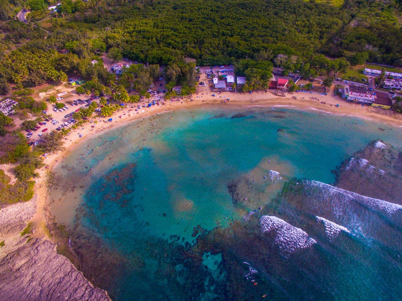 Jobos Beach as seen from above, with many people on the sand and cars visible in the background.