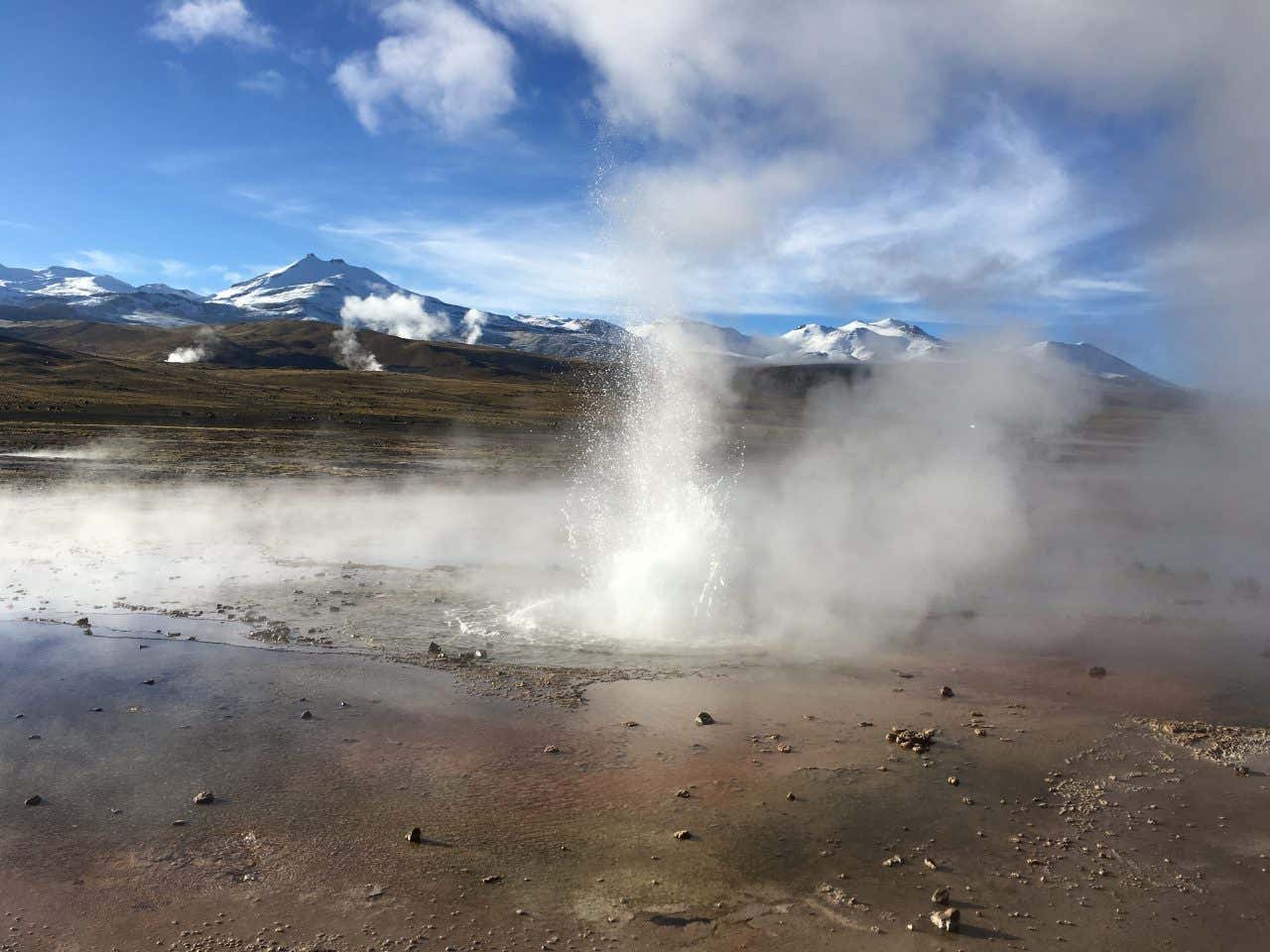 Uma das erupções dos Gêiseres de El Tatio no deserto do Atacama com montanhas ao fundo