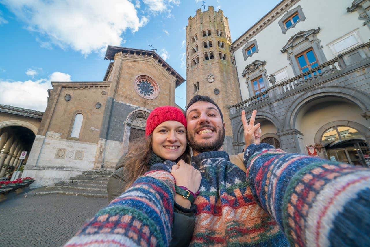 Una giovane coppia, un uomo e una donna, si fanno un selfie nella piazza centrale di Orvieto. Sono vestiti con maglioni e la donna indossa un berretto rosso per ripararsi dal freddo invernale