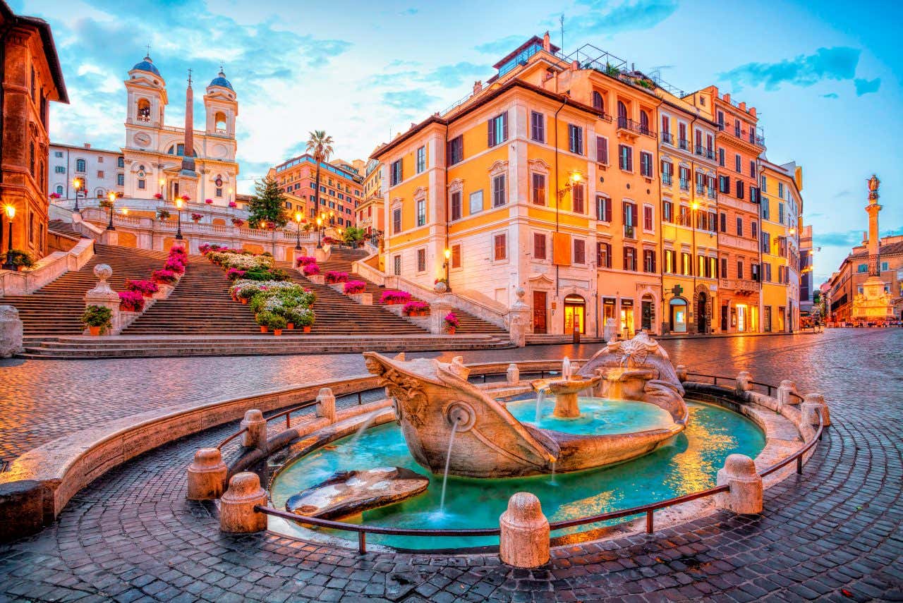 A fountain in Piazza di Spagna in front of the square's famous staircase with the Trinità dei Monti church in the background.