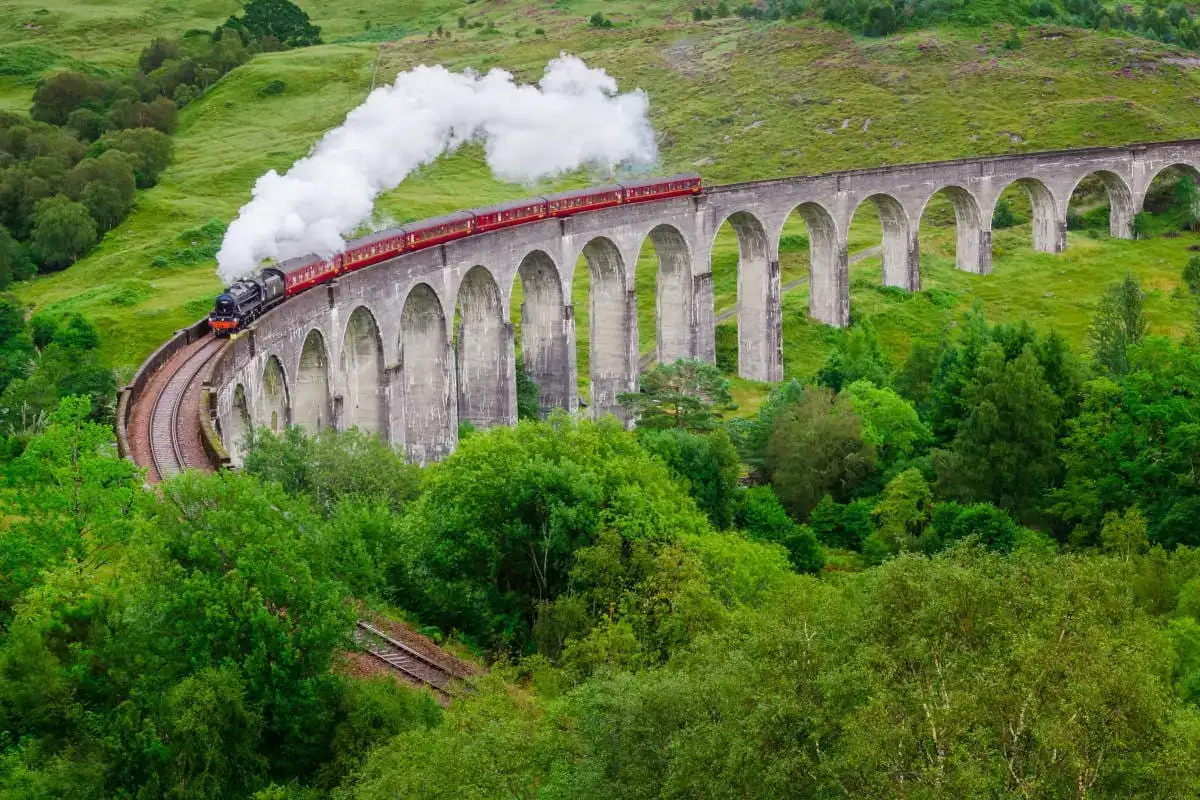 Tren Jacobita rojo humeante en la vía elevada sobre un paisaje boscoso