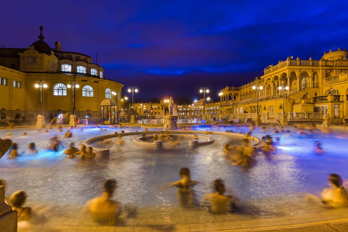 Varias personas nadando en una de las piscinas al aire libre del balneario Széchenyi por la noche