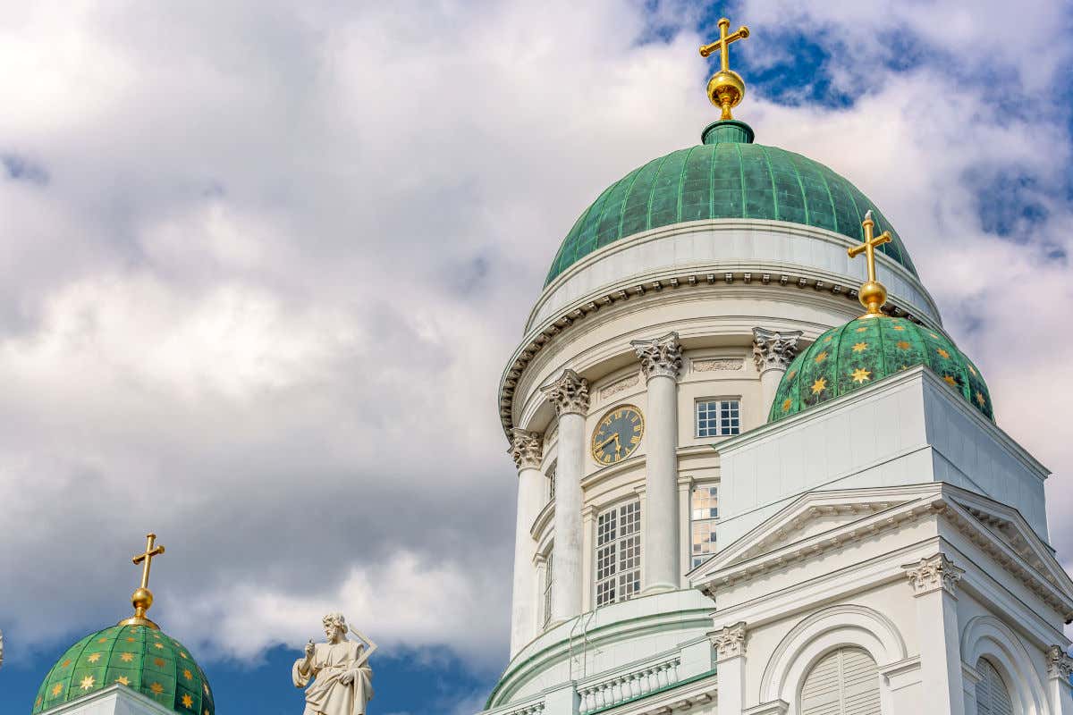 Cúpulas verdes con estrellas y cruces doradas en la catedral de Helsinki, un edificio de color blanco impoluto y decorado con esculturas y un reloj