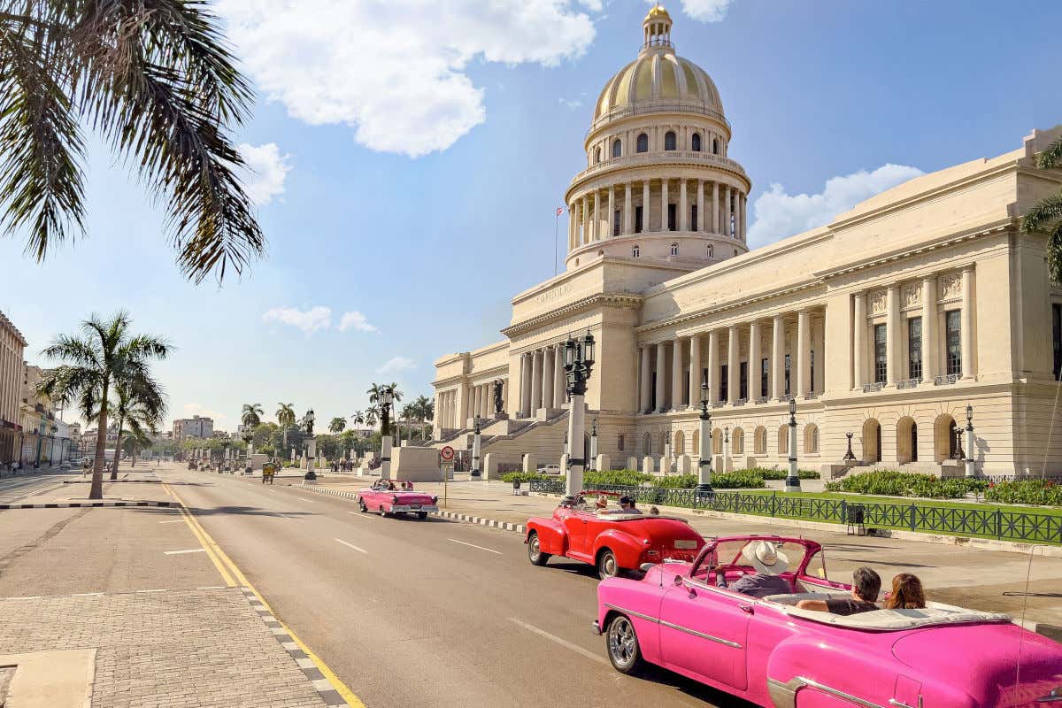 Varios coches clásicos de vivos colores circulando en un día despejado frente a la cúpula del Capitolio de La Habana