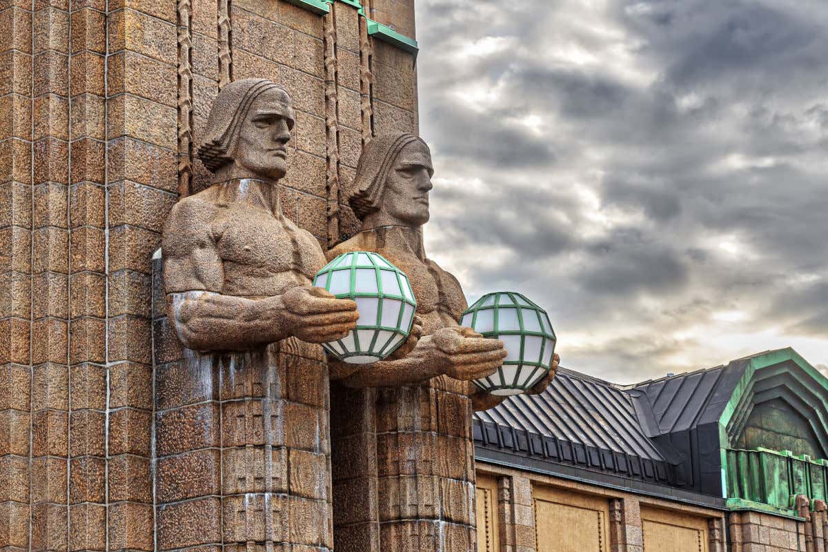 Dos enormes esculturas de piedra sujetando unas lámparas en los exteriores de la estación central de trenes de Helsinki