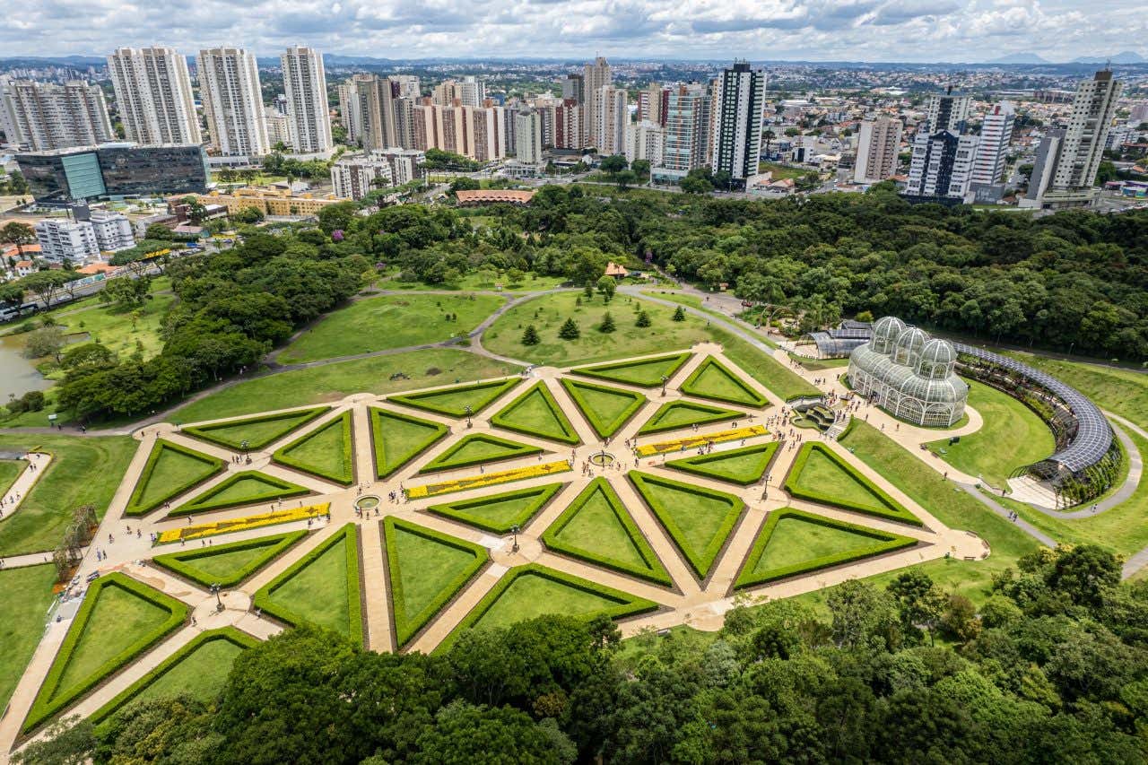 Vista aérea da Estufa de Vidro com os geométricos Jardins Franceses com os prédios de Curitiba ao fundo