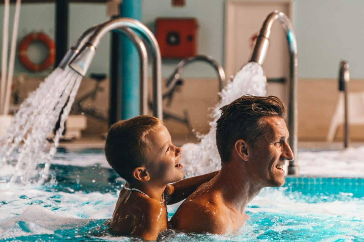 Un padre nadando con su hijo en una piscina termal rodeada de chorros que expulsan agua a alta presión