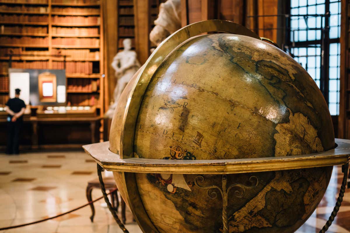 Un globo terráqueo de aspecto antiguo rodeado de estanterías y esculturas en una biblioteca austríaca