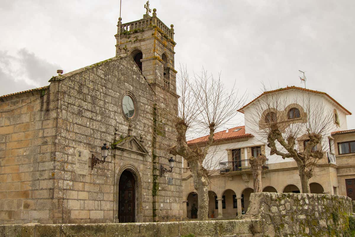 Igrexa de San Miguel de Bouzas, a small stone church next to trees that have no leaves on a cloudy day