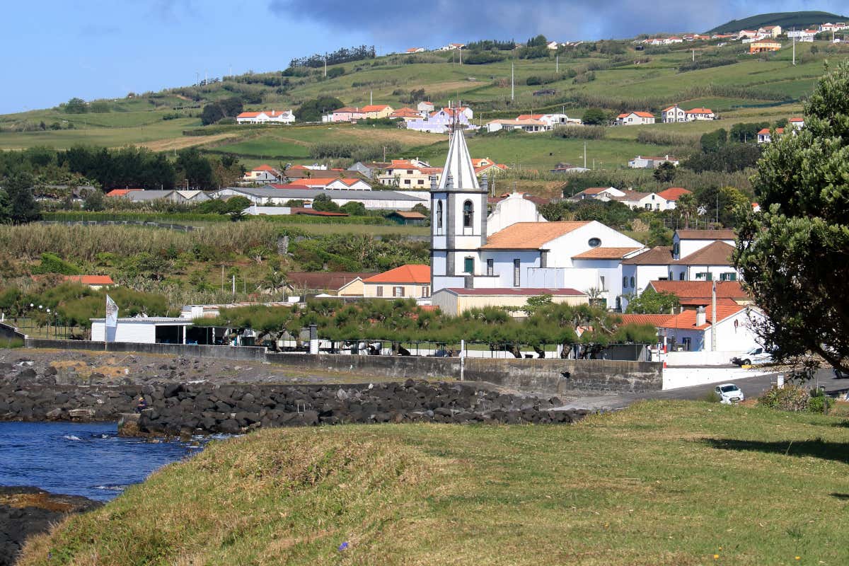 Iglesia encalada de color blanco situada a orilla del mar, con un paisaje verde de fondo