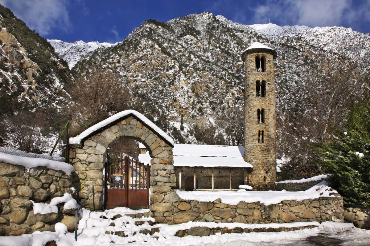 Iglesia de Santa Coloma, un templo religioso de piedra con una torre circular y nieve alrededor