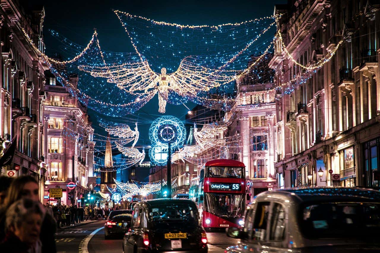 A busy road in London with black cabs and red double decker buses decorated with Christmas lights