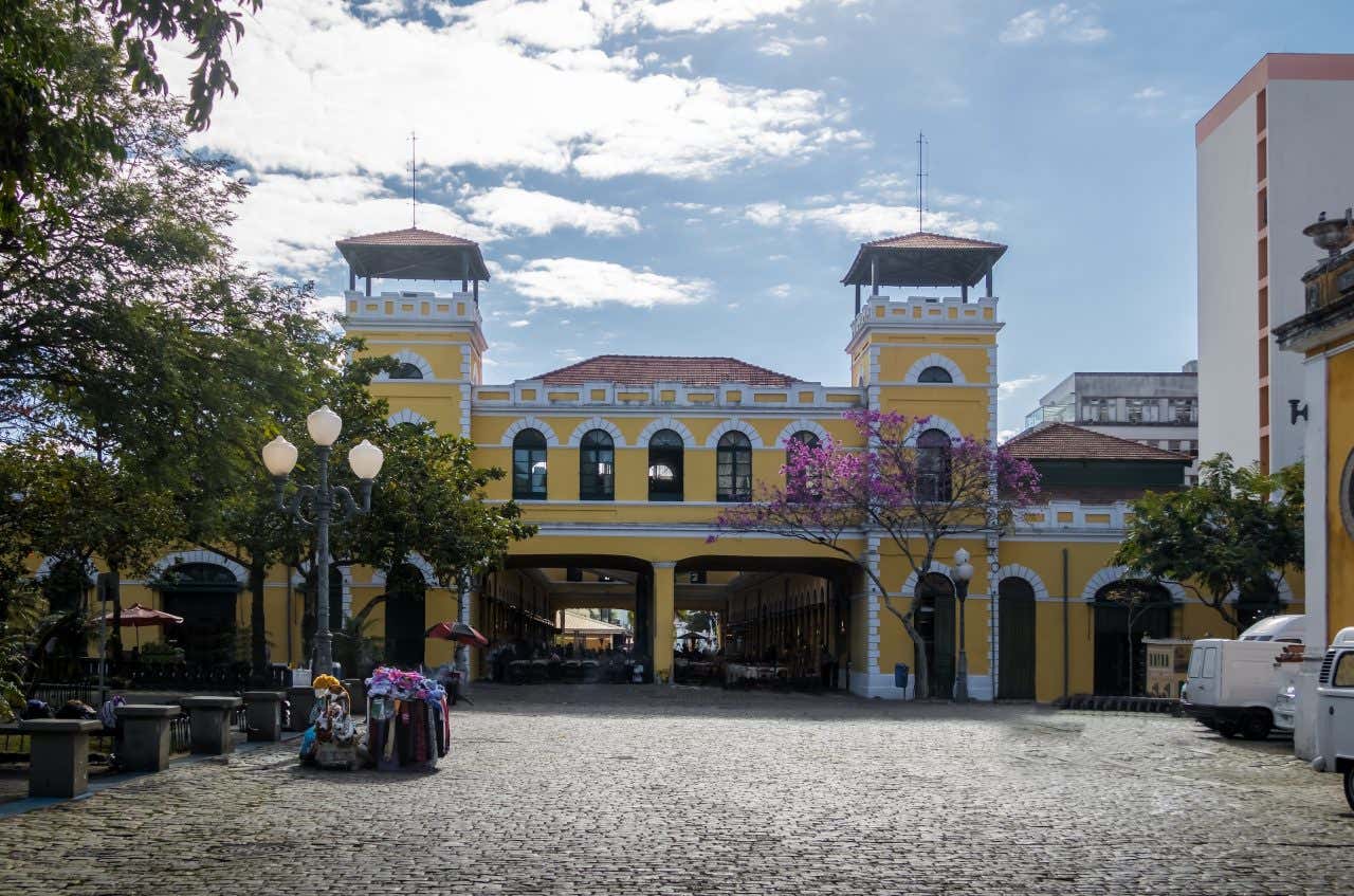 Fachada colonial amarela e branca do Mercado Público de Florianópolis em uma rua de paralelepípedos