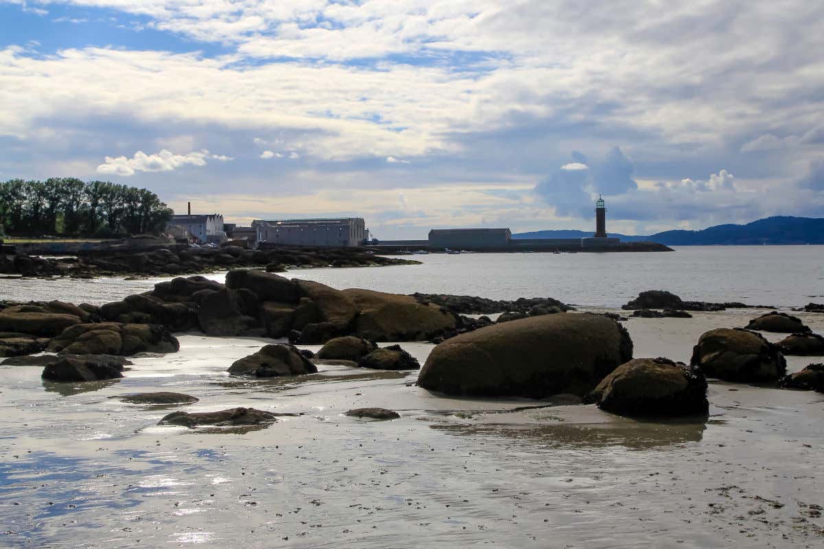 Rocks on a shore with a lighthouse and buildings in the distance