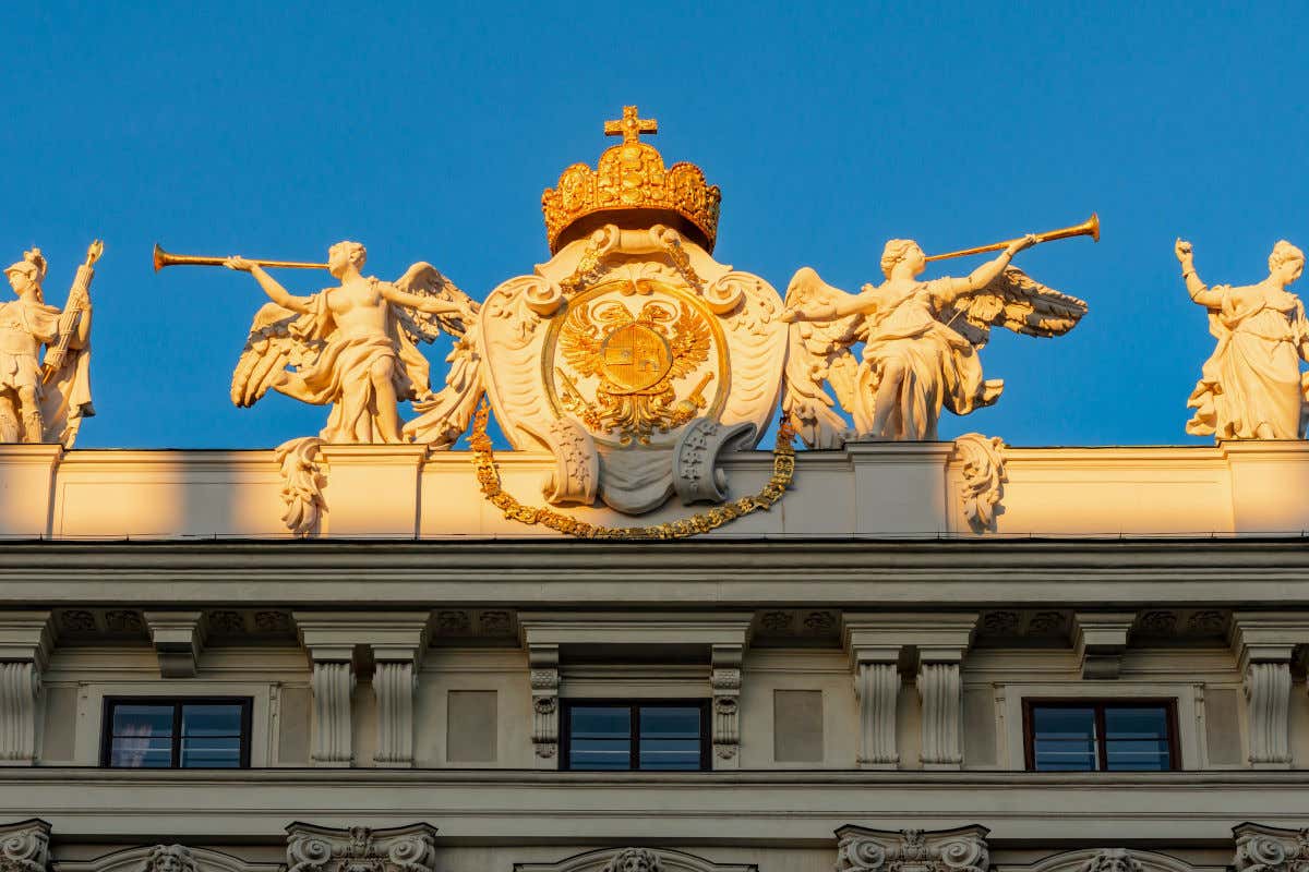 Esculturas de dos ángeles con trompetas rodeando un escudo en los exteriores de un edificio