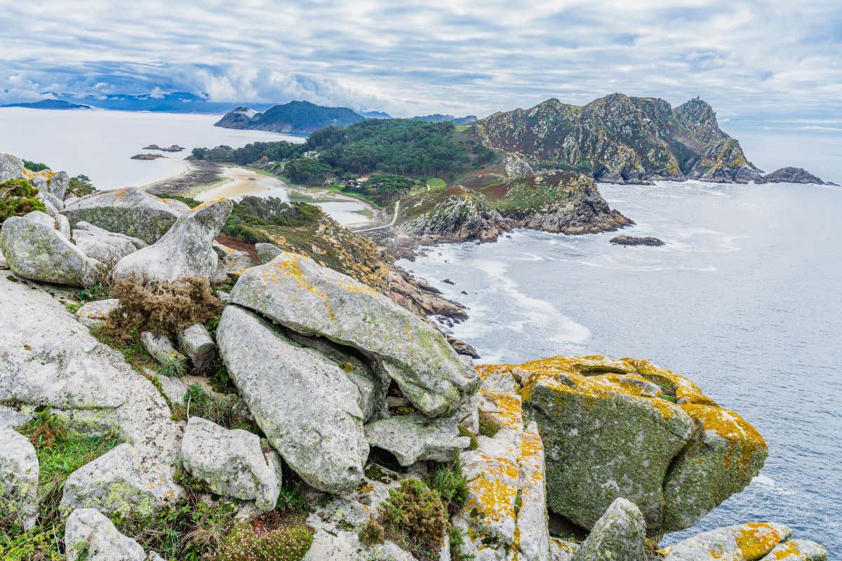 Rocks emerging from the sea with mountains in the distance on a partly cloudy day