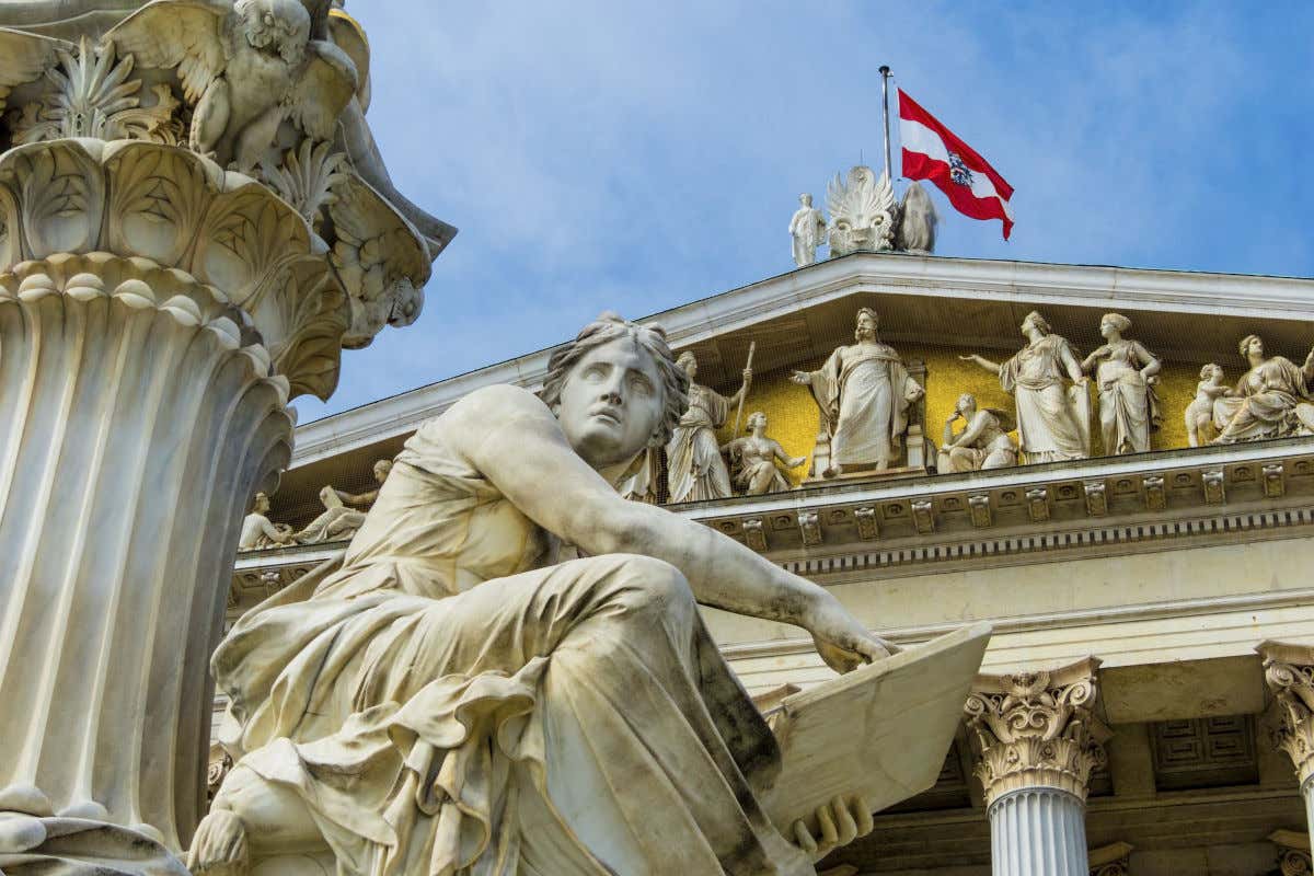 Una escultura clásica de una mujer sentada junto a una columna de capitel corintio frente al Parlamento de Austria