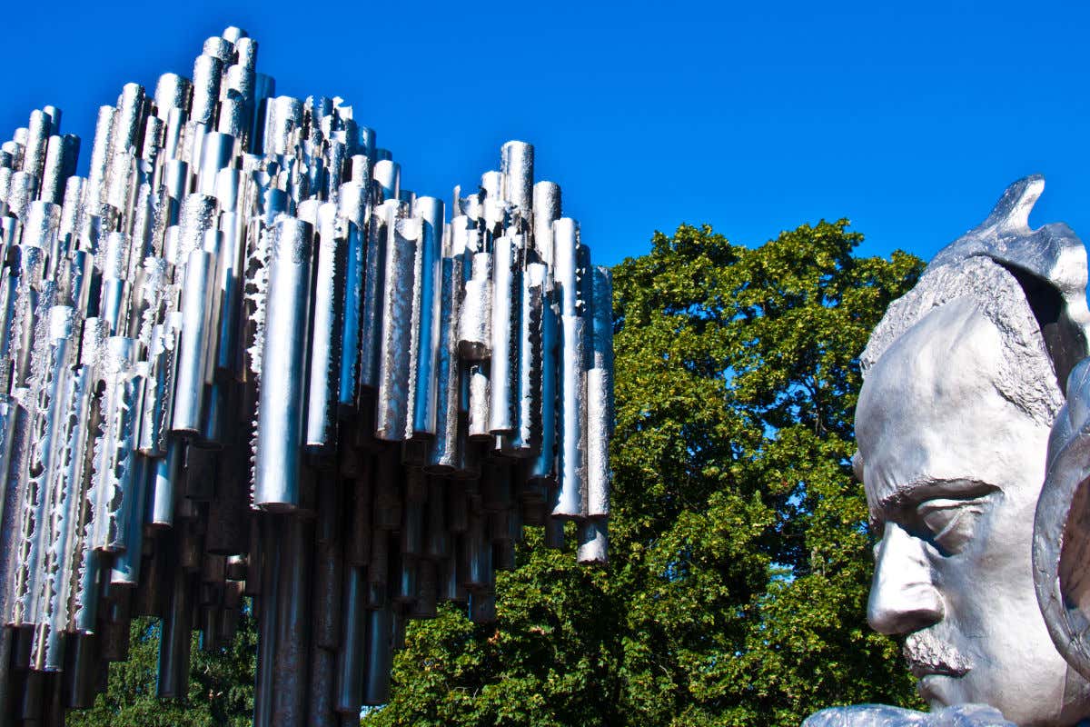 Árboles en el parque Sibelius de Helsinki con una escultura con rostro humano y otra formada por tubos cilíndricos