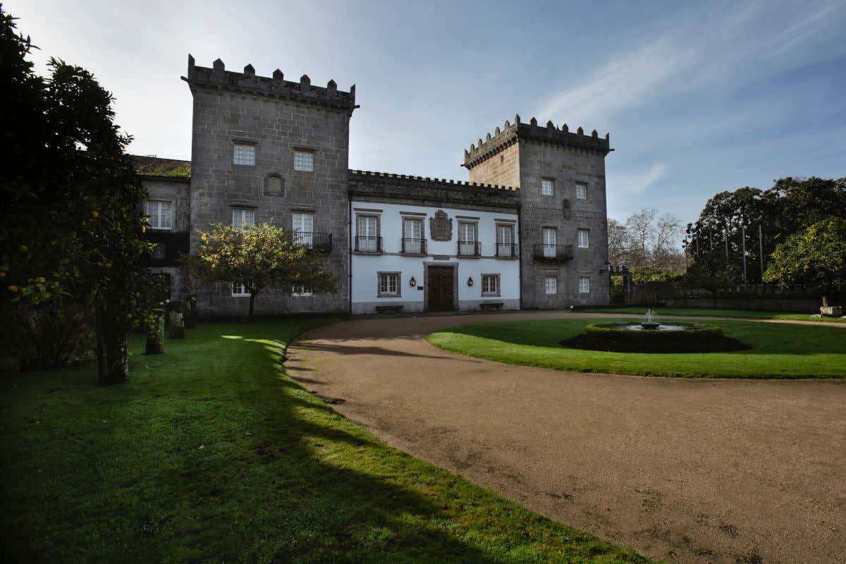 A palace with two stone towers and a garden with a fountain in front on a sunny day