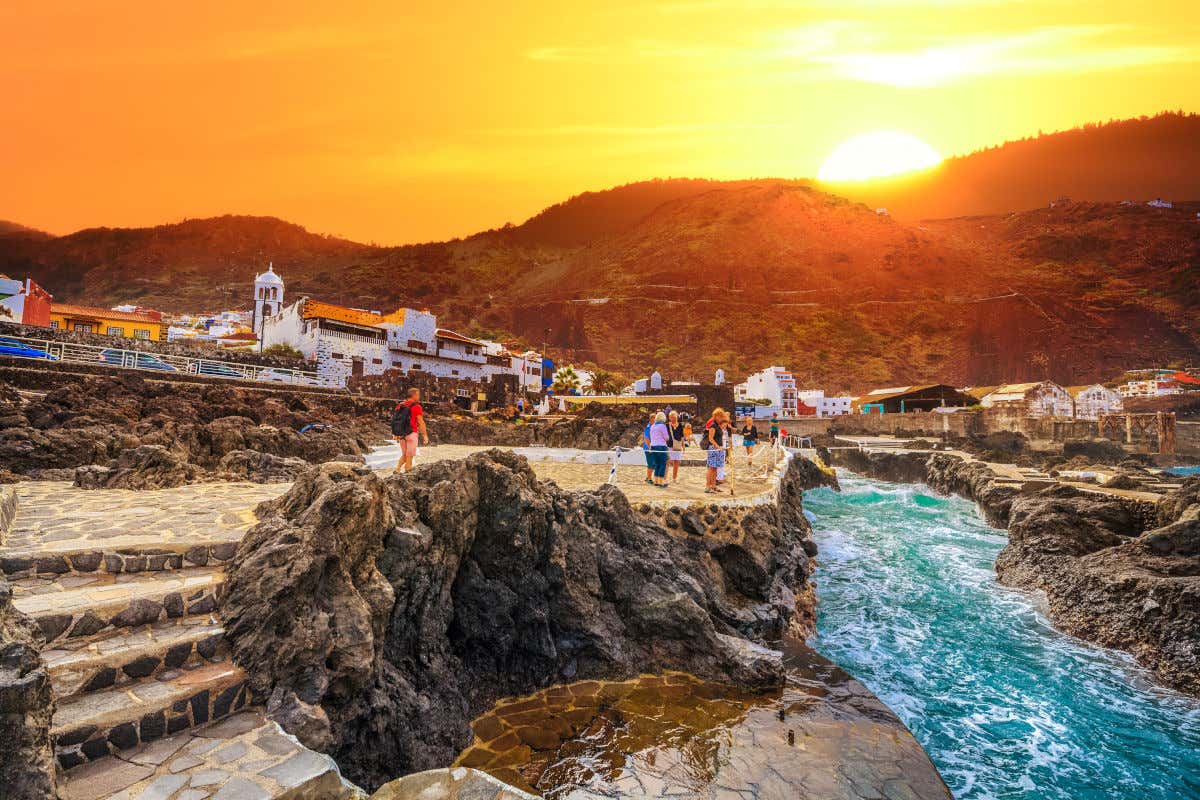 Atardecer entre las montañas y frente a una costa rocosa con varias personas contemplando el mar