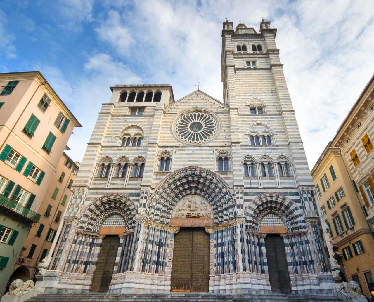 Vista dal basso della facciata di una chiesa gotico-romanica decorata con file di mattoni in pietra bianca e nera alternate tra loro in orizzontale. La facciata riporta al primo piano anche diverse sculture sul portone di entrata e sui capitelli dei colonnati che ornano le due porte laterali