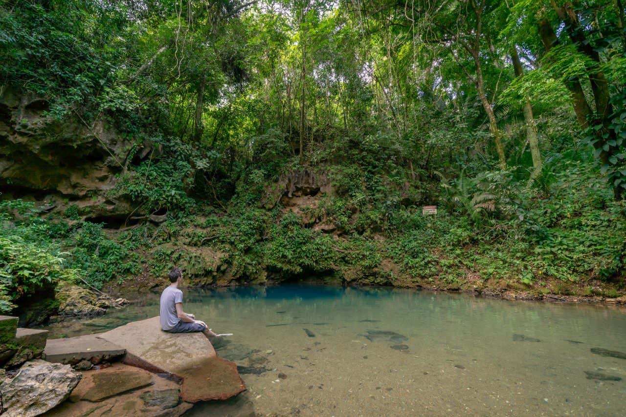 The large cenote in Blue Hole National Park, with a man sitting to the left on a rock.