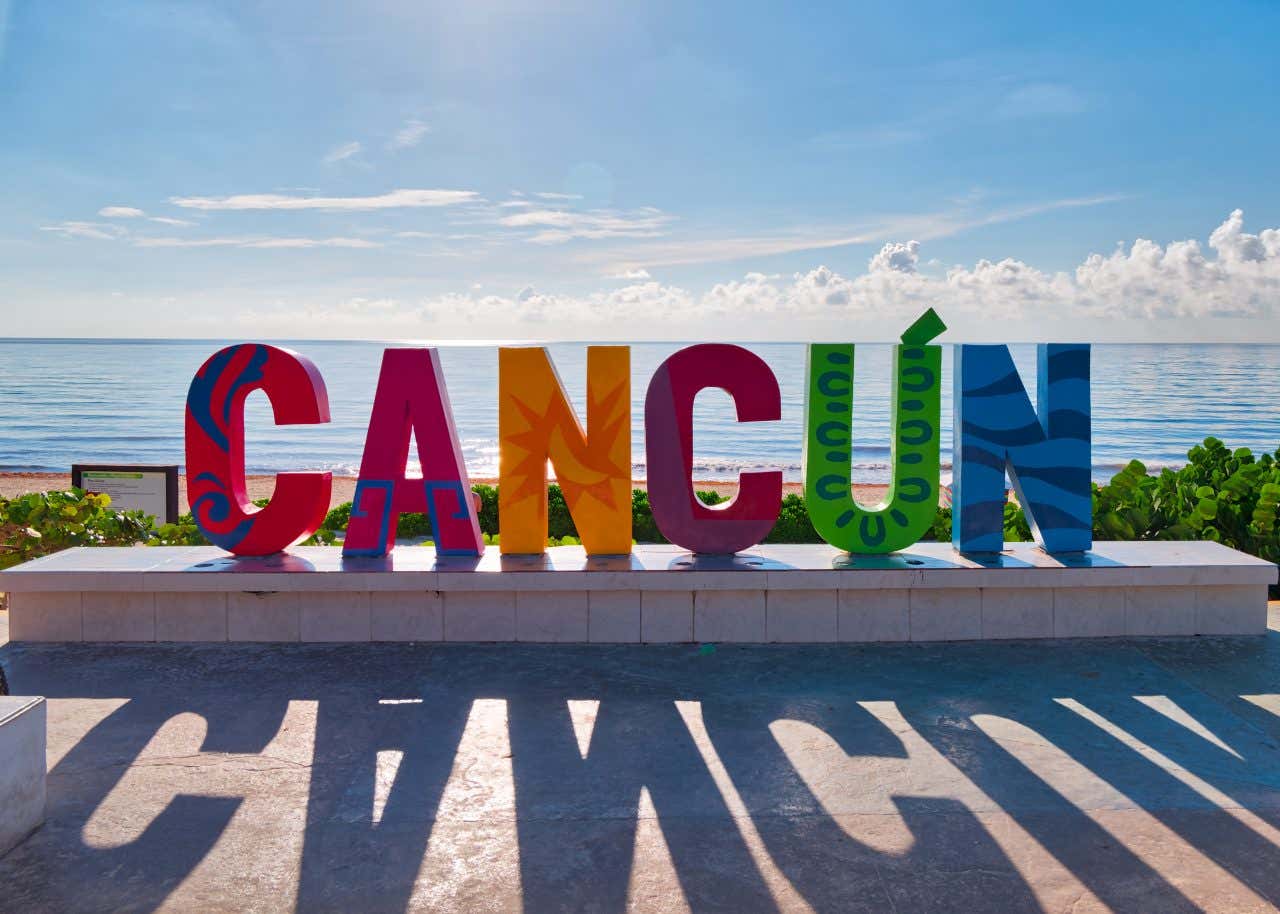 Um letreiro multicolorido de Cancún com um céu azul nublado ao fundo