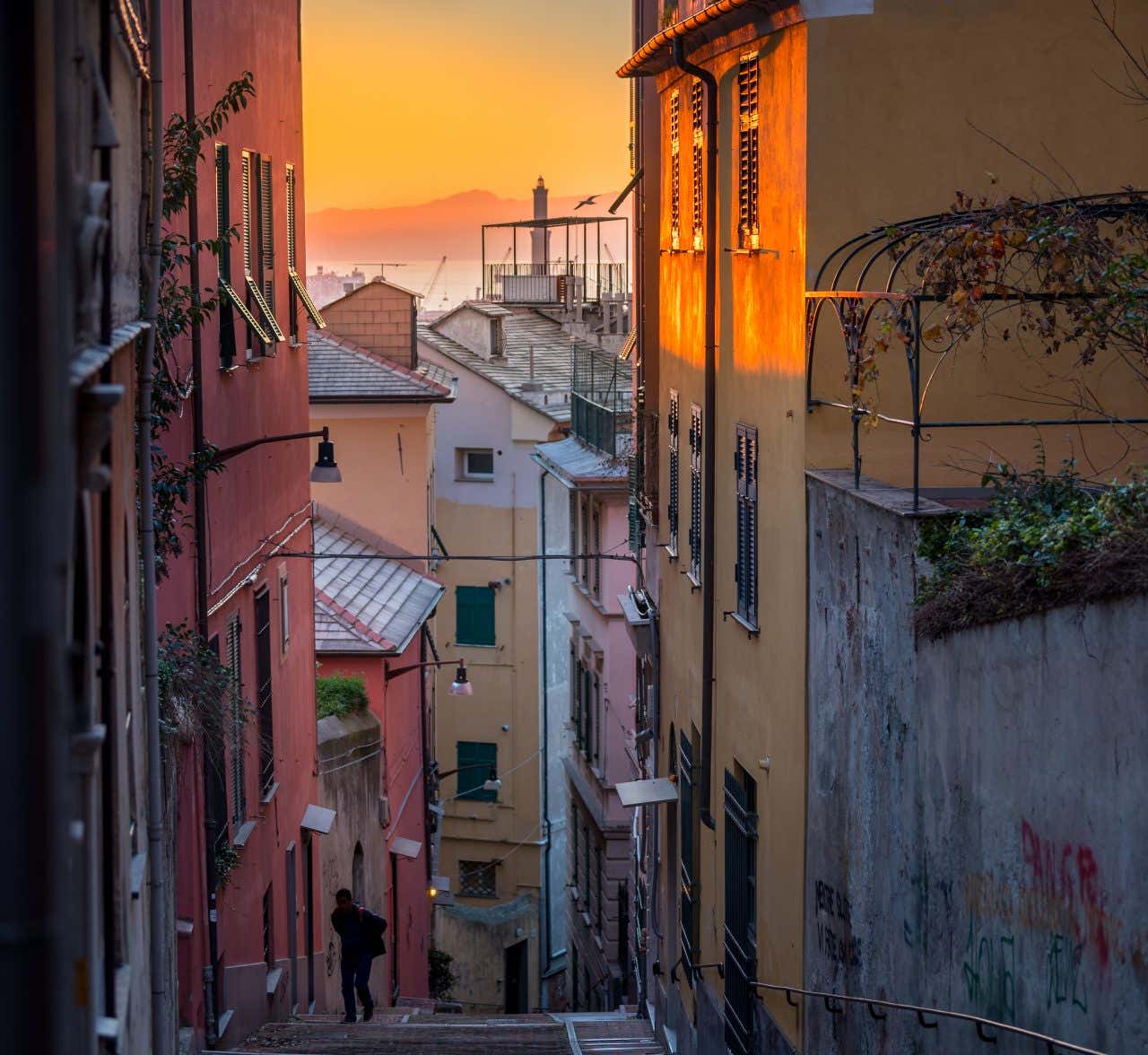 Uma rua íngreme entre prédios coloridos ao anoitecer. Uma pessoa está subindo a rua, uma das atividades imperdíveis que fazer em Gênova