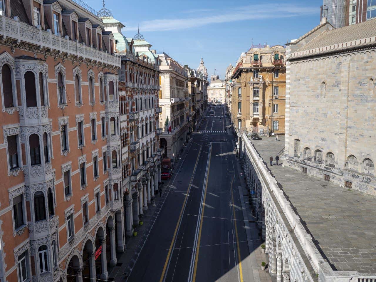 Una via urbana ripresa dall'alto. Si vede una strada asfaltata con diverse corsie stretta tra alti palazzi di diverse epoche e colori