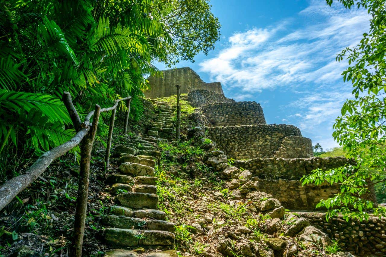 Caracol Temple as seen from below with a staircase in the foreground and a cloudy blue sky in the background.