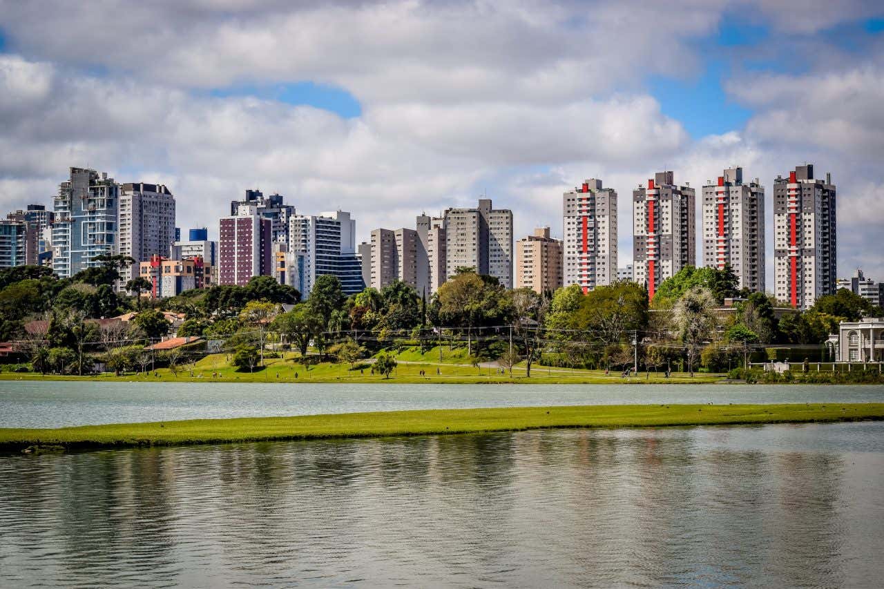 Paisagem do rio Barigui com os edifícios de Curitiba ao fundo em um dia ensolarado